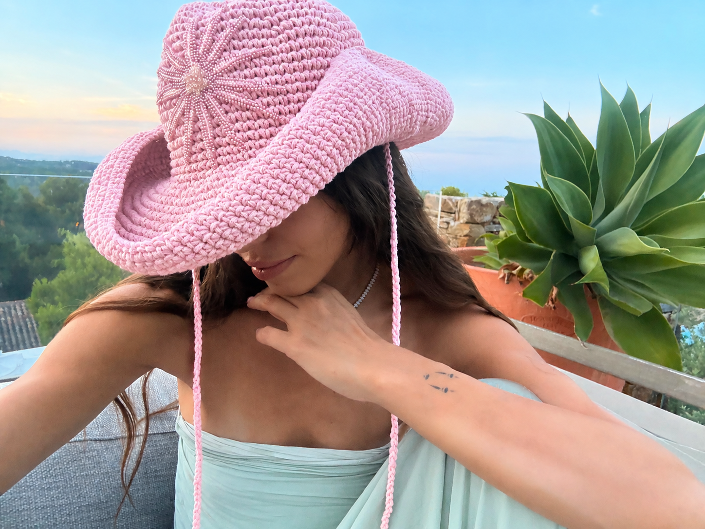 Hand-crocheted baby pink cotton sun hat with beaded sunburst embroidery and an oversized brim, the perfect luxury accessory for summer holidays and beach vacations.